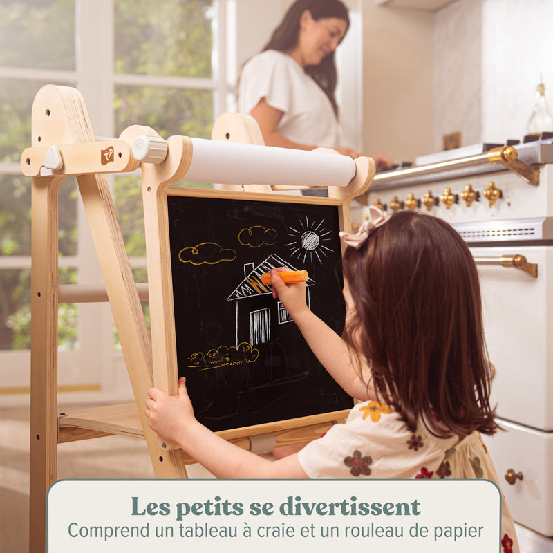 Une enfant dessine sur le tableau créatif de la tour d’apprentissage, comprenant un tableau à craie et un rouleau de papier.
