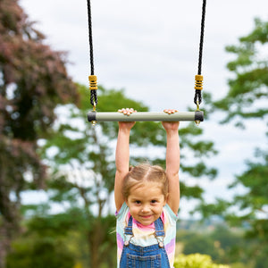 Une enfant se suspend au trapèze en métal TP Toys, conçu pour développer coordination, force et équilibre.