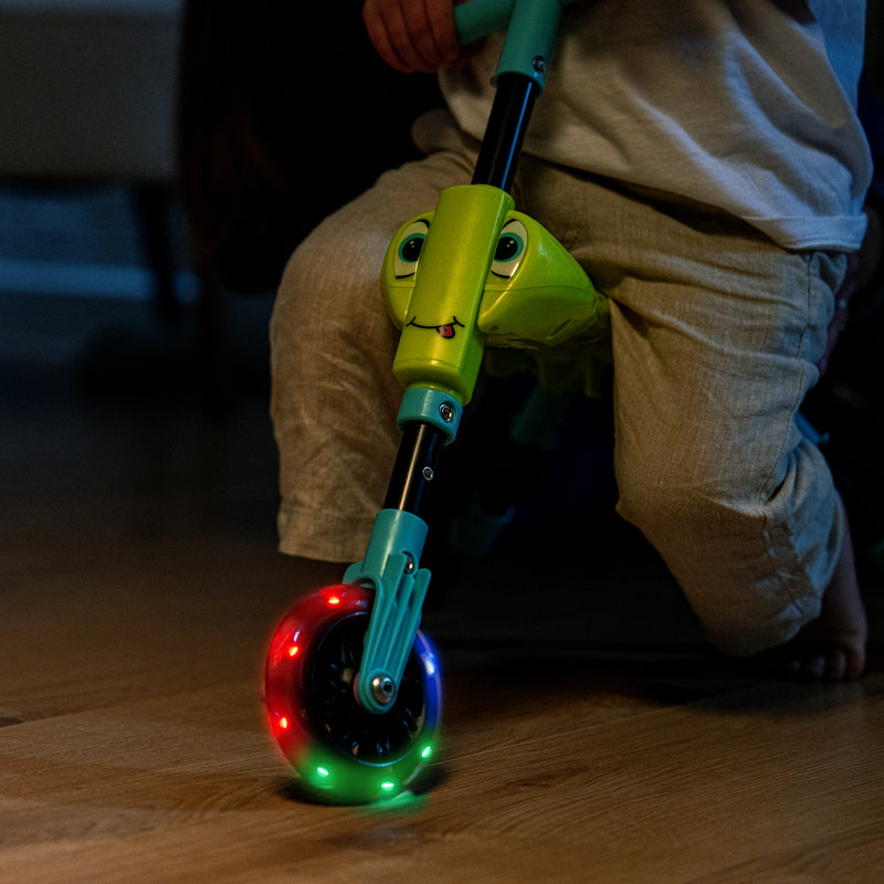Gros plan sur la roue avant lumineuse d’un tricycle pour enfant, avec des LED colorées allumées pendant qu’un enfant roule à l’intérieur.