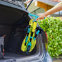 Une personne place un tricycle plié pour enfant dans le coffre d’une voiture, montrant son format compact et facile à transporter.