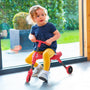 Une enfant est assise sur le tricycle pliable SCUTTLEBUG BEETLE rouge et noir, utilisé en intérieur.