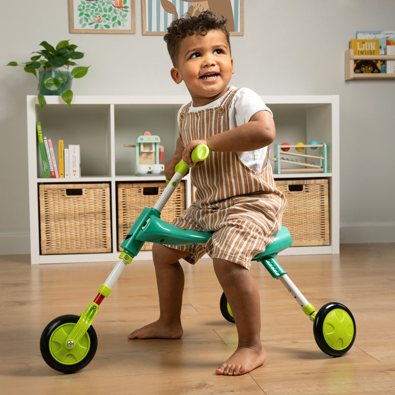 Un enfant est assis sur le tricycle SCUTTLEBUG XL hauteur réglable bleu et vert.