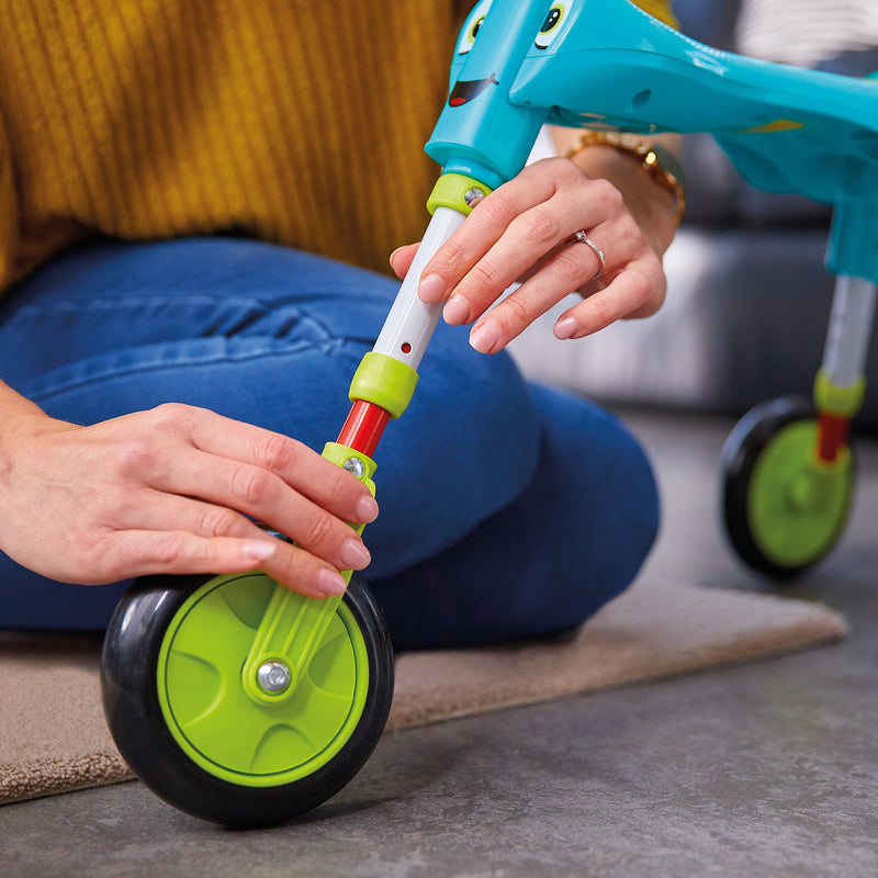 Un adulte assemble le tricycle SCUTTLEBUG XL hauteur réglable bleu et vert.