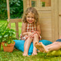 Une enfant est assise devant la maisonnette en bois.