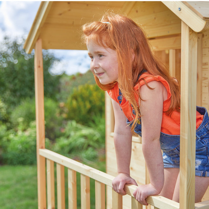 Une enfant se tient sur le balcon d’une cabane en bois sur pilotis.