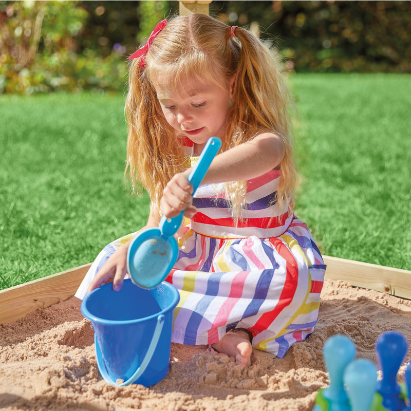Une enfant joue dans un bac à sable avec une pelle et un seau.